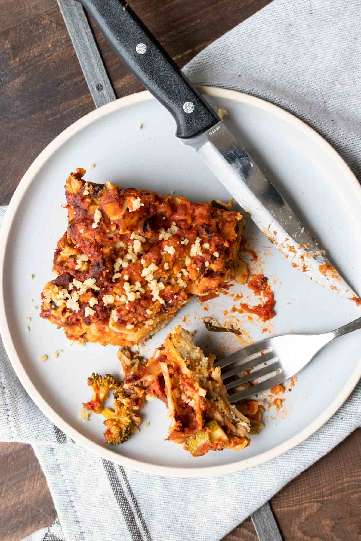 Top view of a piece of vegetable lasagna on a white plate with a bite cut out.