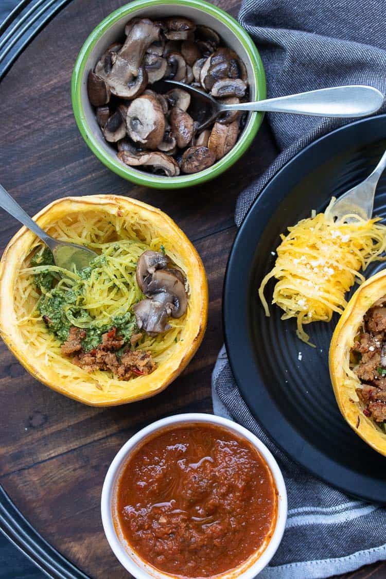 Baked spaghetti squash half being topped with mushrooms, marinara and pesto