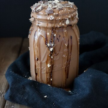 A vegan peanut butter cup milkshake with chocolate overflowing from the top of a mason jar