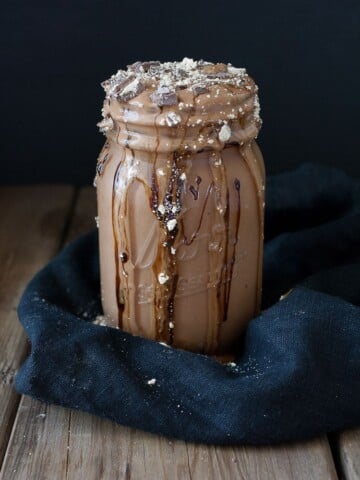 A vegan peanut butter cup milkshake with chocolate overflowing from the top of a mason jar