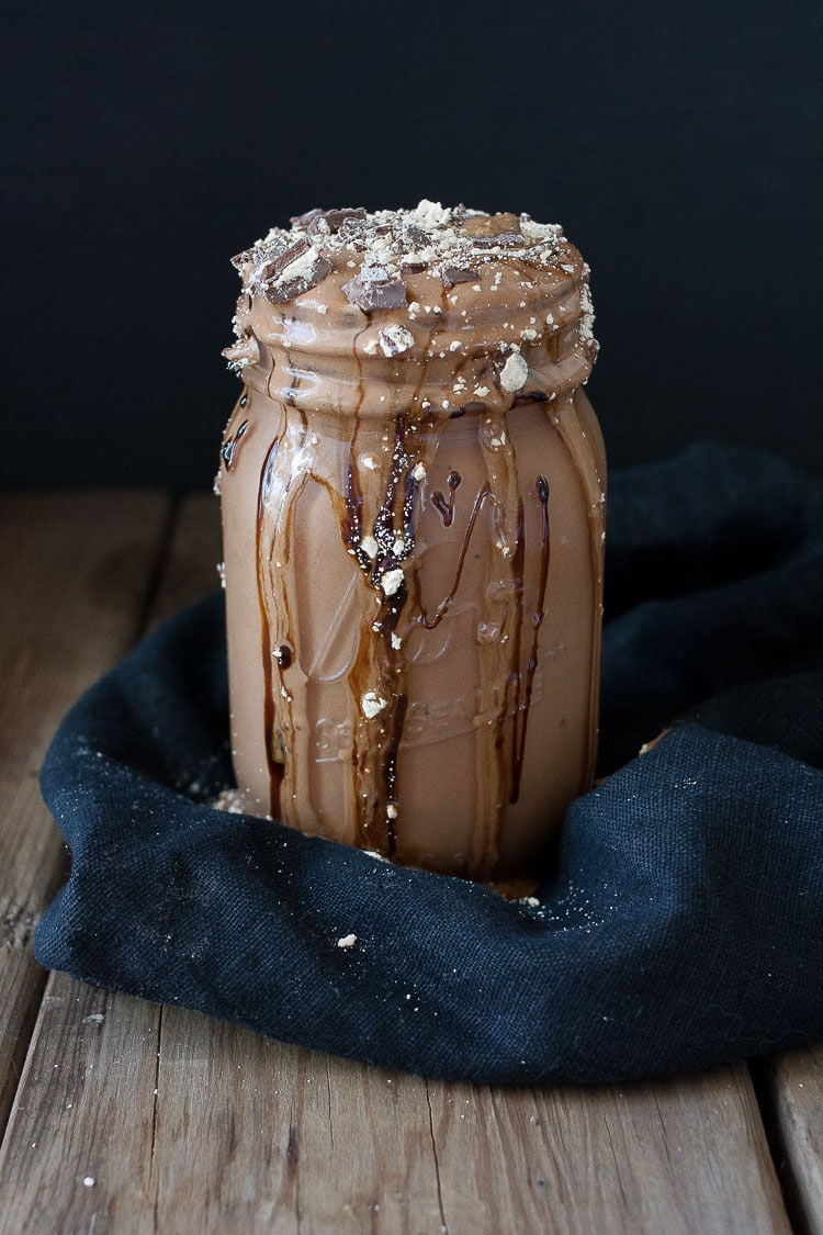 A vegan peanut butter cup milkshake in a mason jar with chocolate overflowing from the top