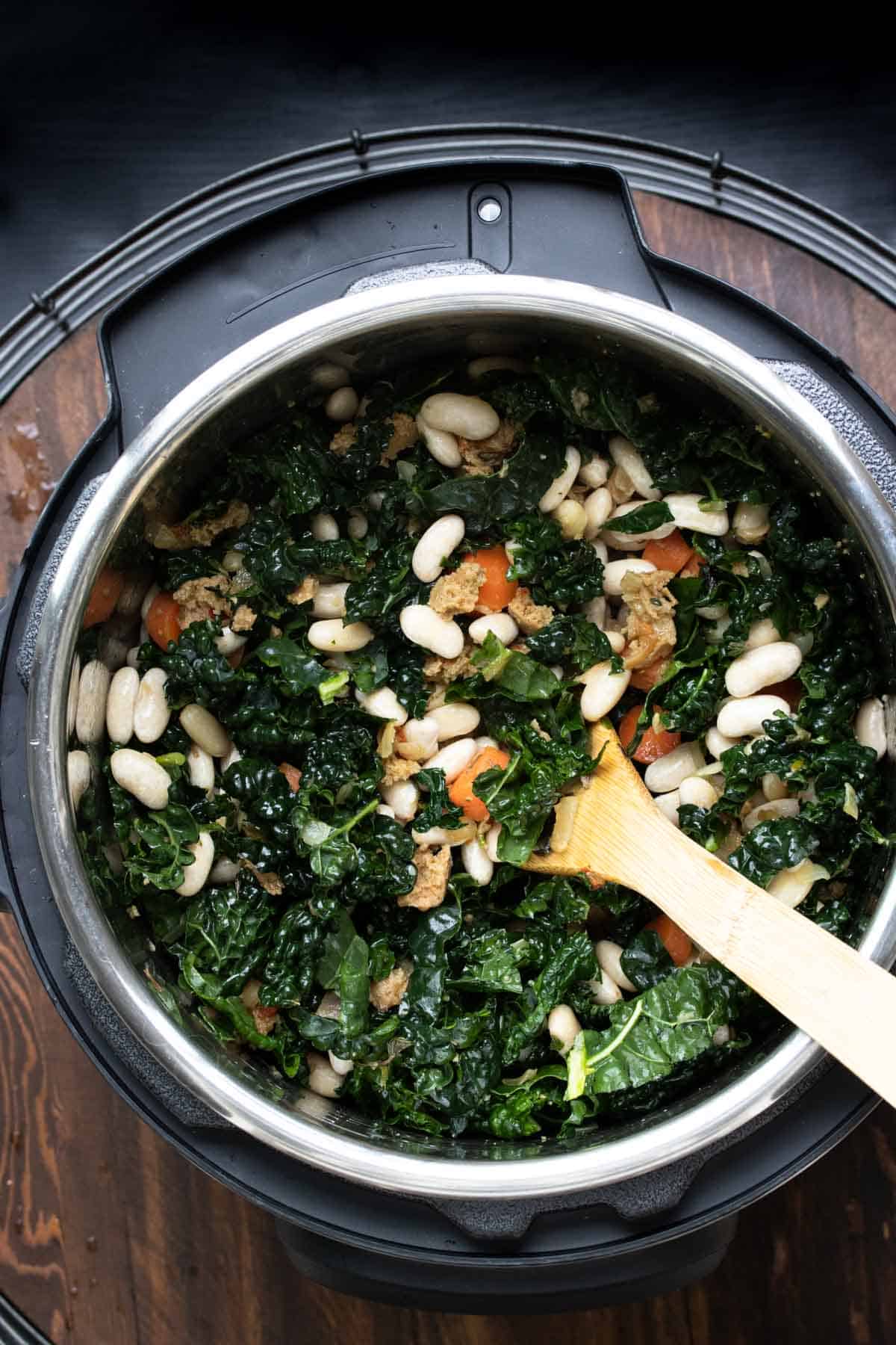 Top view of kale, white beans, carrots and sausage being mixed in an instant pot.