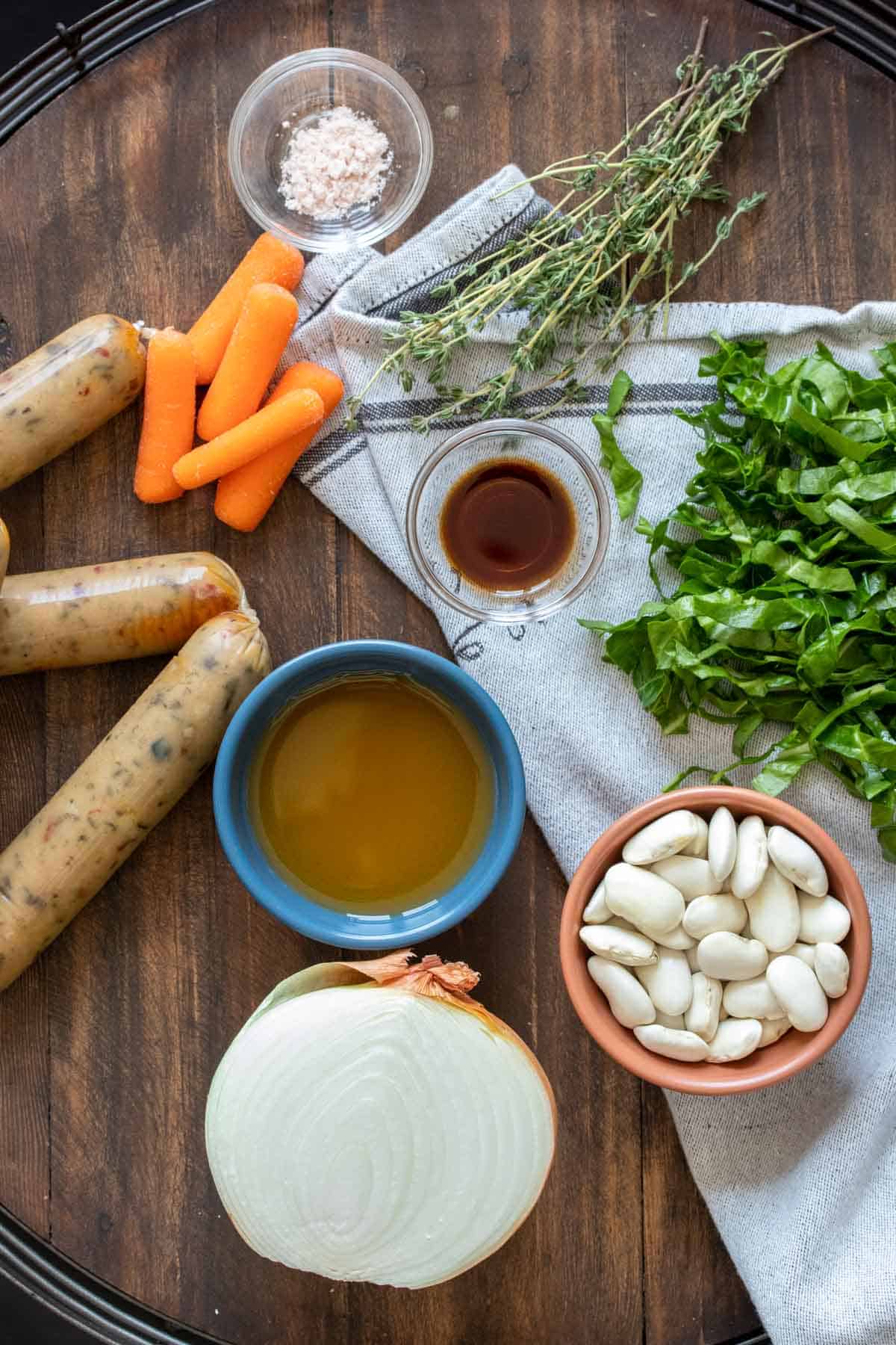 Ingredients needed to make a bean, kale and sausage soup on a wooden surface.