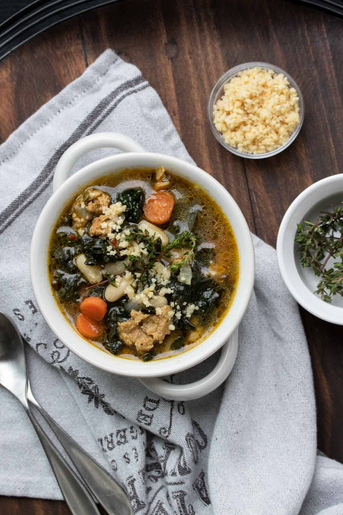 Top view of sausage, kale, white bean and carrot soup on a grey napkin.