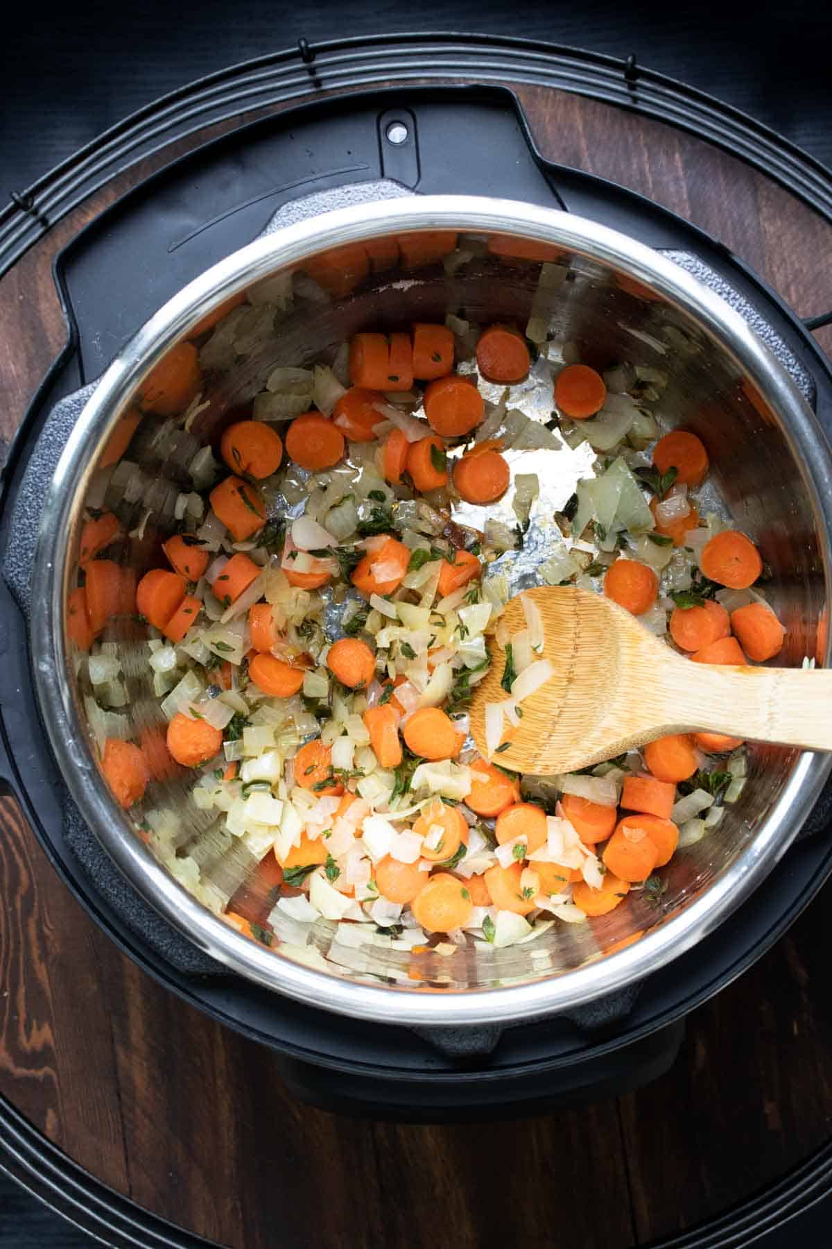 Top view of carrots, onions and herbs sautéing in an instant pot.