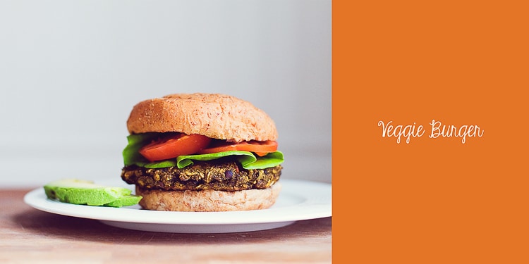 A veggie bean burger sitting on a white plate with tomato and lettuce and veggie burger written in text at the side