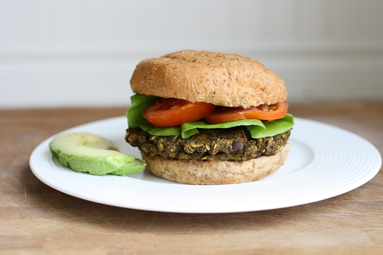 A veggie bean burger on a bun with tomato and salad on a white plate