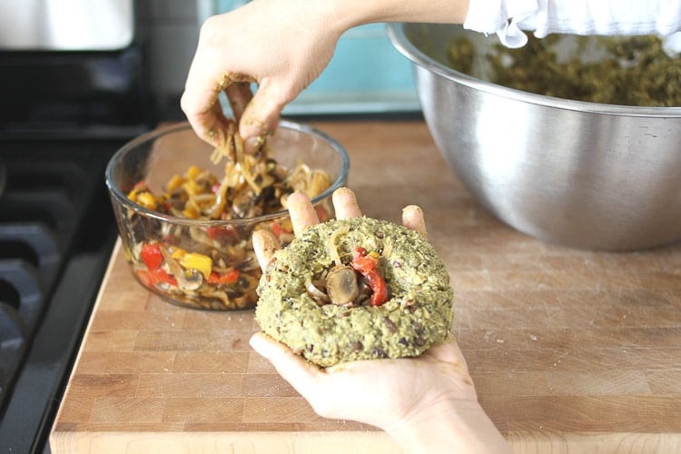 A hand holding a Stuffed Veggie and Bean Burger and filling it with stuffing