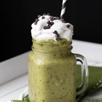 Green shake with chocolate chips in glass jar topped with whipped cream and a straw