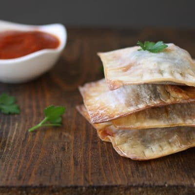 A stack of lasagna wontons on a wooden surface next to dipping sauce