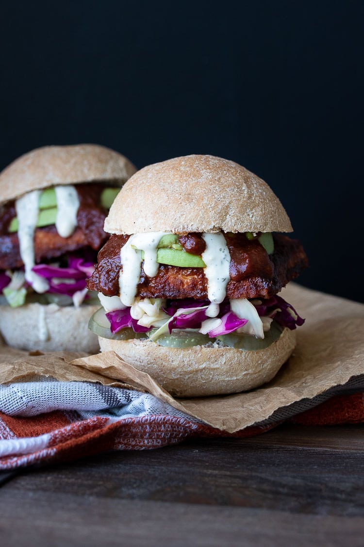Front view of a BBQ tempeh sandwich in a bread roll with cabbage, avocado, pickles and ranch