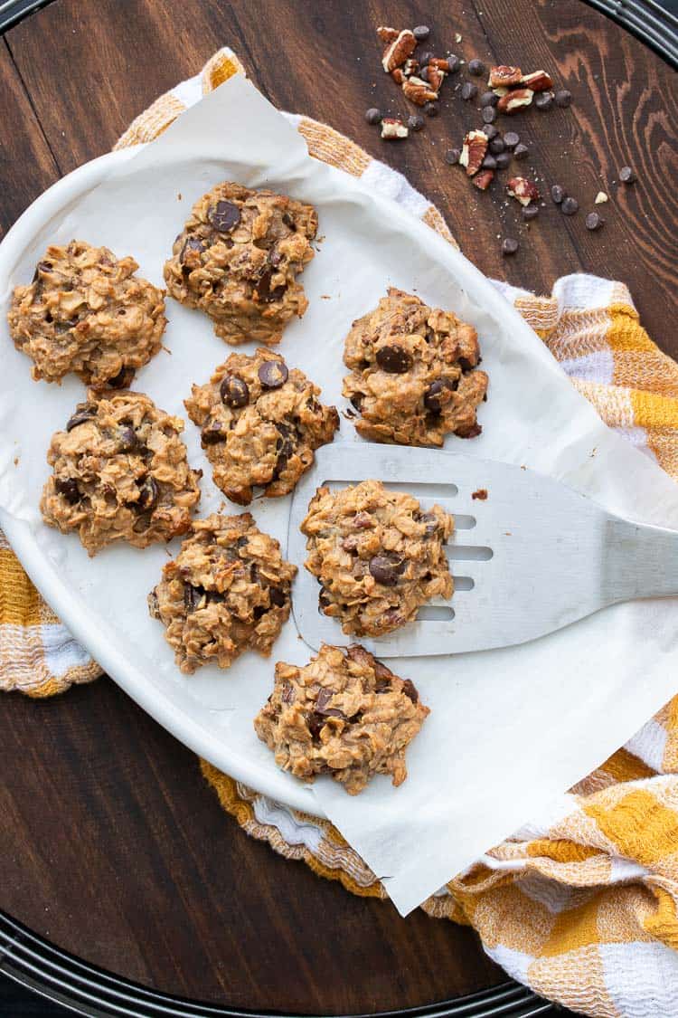 Metal spatula picking up oatmeal chocolate chip cookie off a white plate