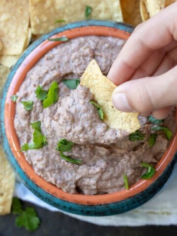 Hand dipping chip into bean dip in a turquoise bowl