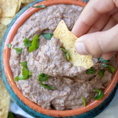 Hand dipping chip into bean dip in a turquoise bowl