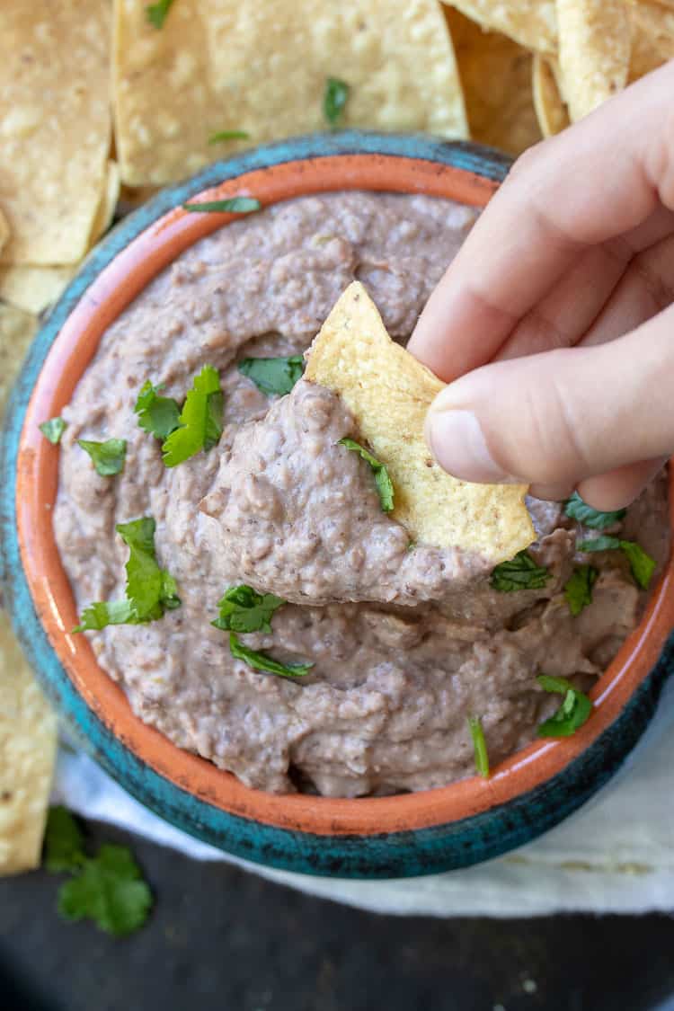 Hand dipping chip into bean dip in a turquoise bowl