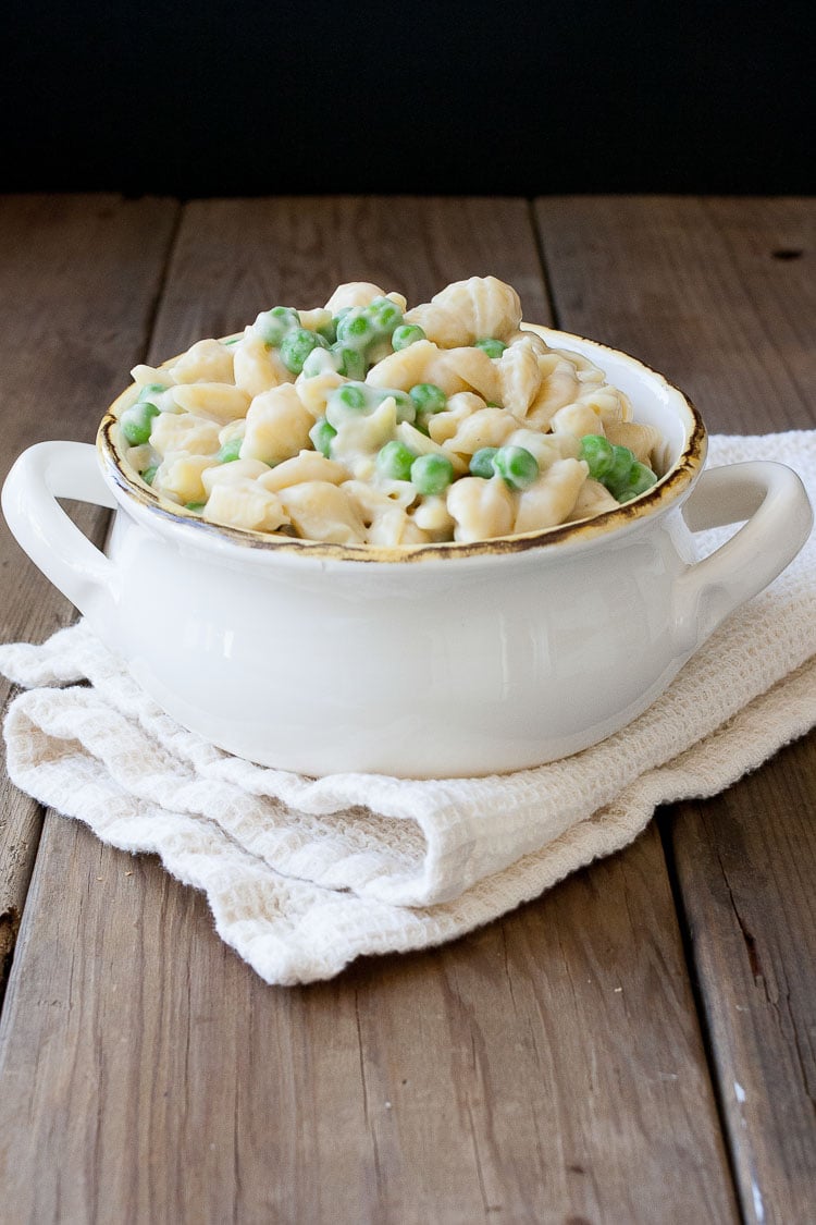 Creamy mac pasta and peas in a white bowl sitting on a wooden surface
