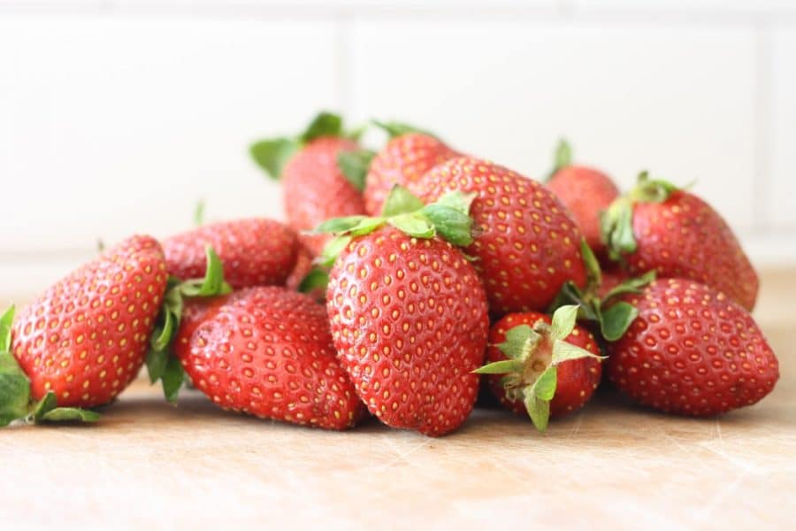 A pile of strawberries on a wooden counter top