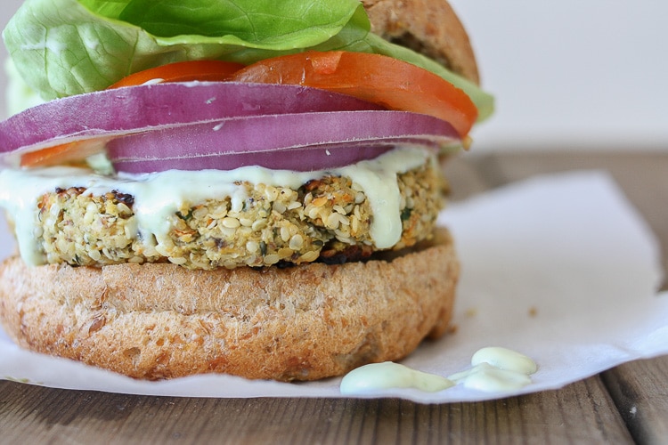 A close up of a cauliflower burger topped with onion, tomato and lettuce sitting on a wooden surface