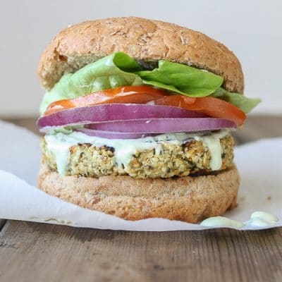 A Cauliflower burger topped with onion, tomato and salad in a burger bun