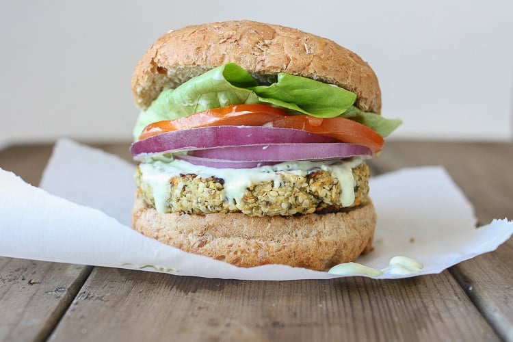 A Cauliflower burger topped with onion, tomato and salad in a burger bun