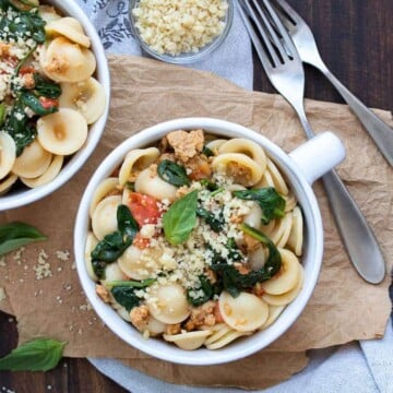 White soup bowl filled with sausage spinach tomato pasta and vegan parmesan