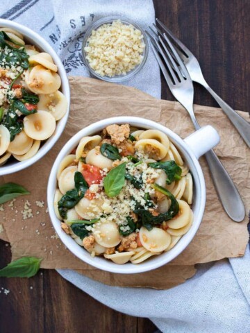 White soup bowl filled with sausage spinach tomato pasta and vegan parmesan