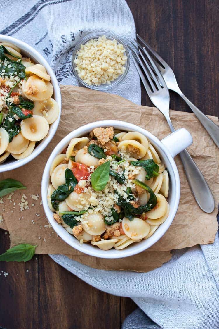 White soup bowl filled with sausage spinach tomato pasta and vegan parmesan