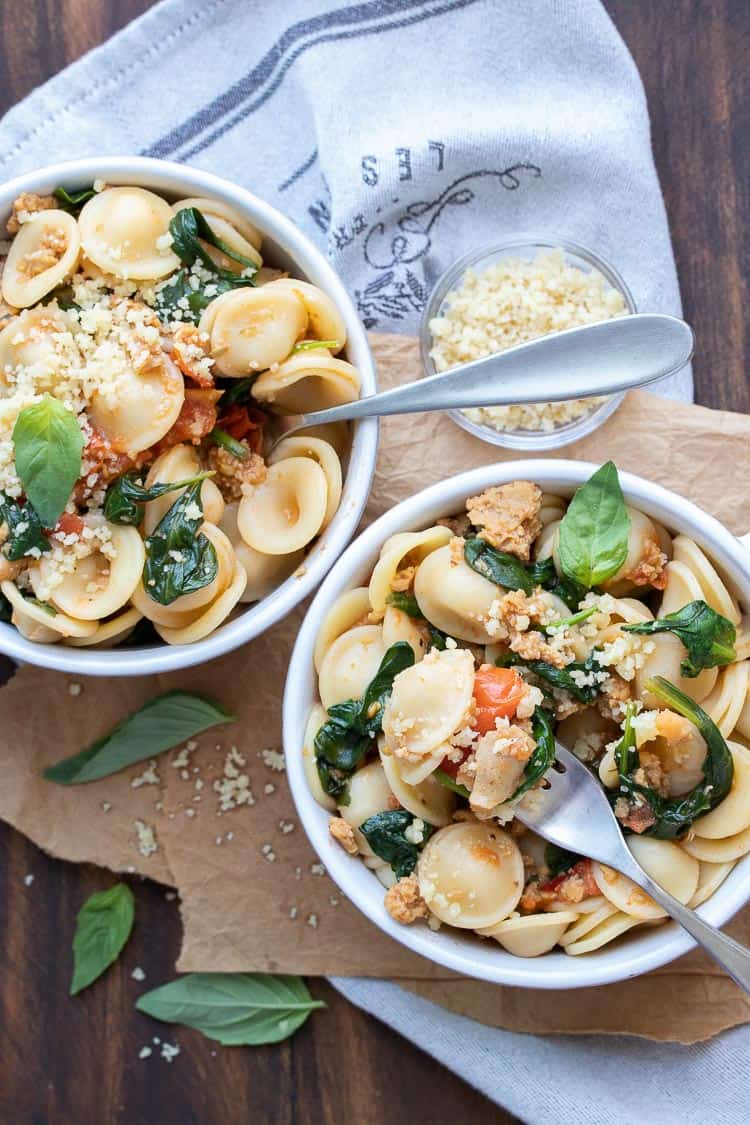Forks scooping bites out of bowls with spinach tomato sausage pasta