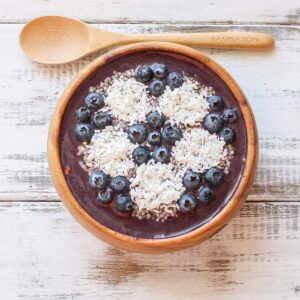 A wooden spoon parallel to a smoothie bowl with a soccer ball design made of blueberries and coconut.