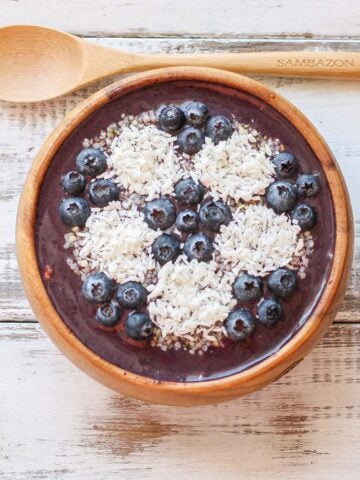 A wooden spoon parallel to a smoothie bowl with a soccer ball design made of blueberries and coconut.