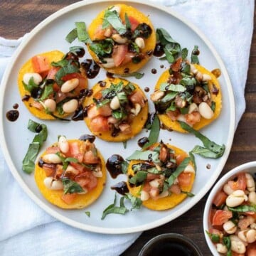 Polenta rounds with tomato white bean bruschetta on top on a white plate