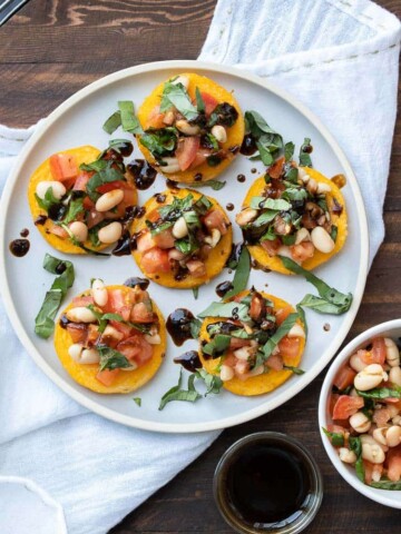 Polenta rounds with tomato white bean bruschetta on top on a white plate