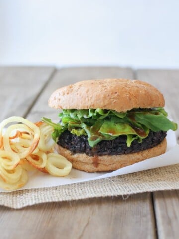 A black rice burger on a wooden surface with onion rings at the side