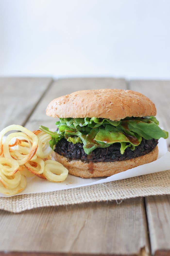 Black rice burgers on a bun with lettuce and onion rings at the side