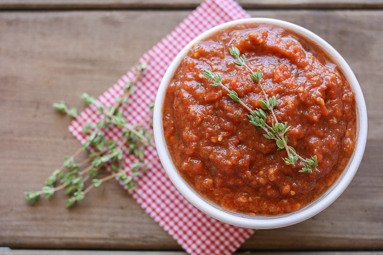 An overhead shot of raw marinara sauce in a white bowl sitting on a wooden surface