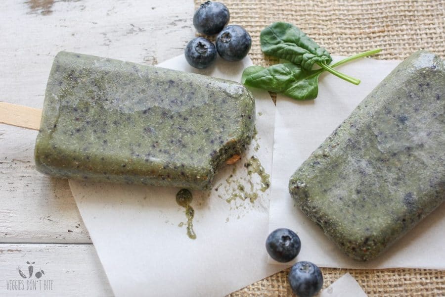 A close up shot of healthy breakfast popsicles sitting on a wooden surface with blueberries