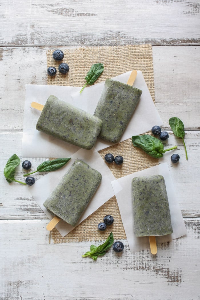 An overhead shot of healthy breakfast popsicles on a wooden surface with berries scattered around