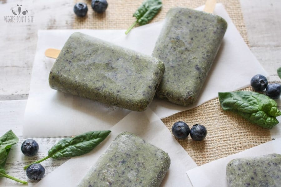 Healthy breakfast popsicles laying on a wooden surface with berries and spinach leaves scattered around