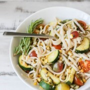 A side shot of linguine with summer vegetables in a white bowl with a fork