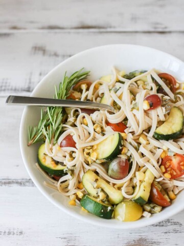 A side shot of linguine with summer vegetables in a white bowl with a fork