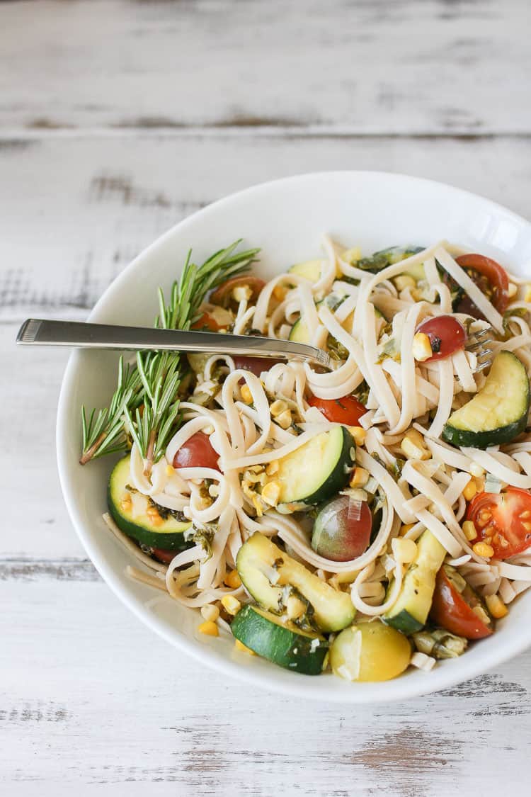 A side shot of linguine with summer vegetables in a white bowl with a fork