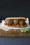 Vegan beanball sub with sautéed kale marinara sauce sitting on a wooden cutting board