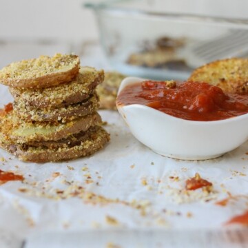 A stack of Hemp Almond Parmesan Potato Chip Rounds on parchment paper with a tomato dipping sauce