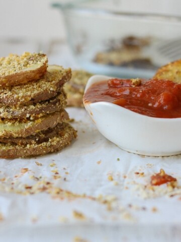 A stack of Hemp Almond Parmesan Potato Chip Rounds on parchment paper with a tomato dipping sauce