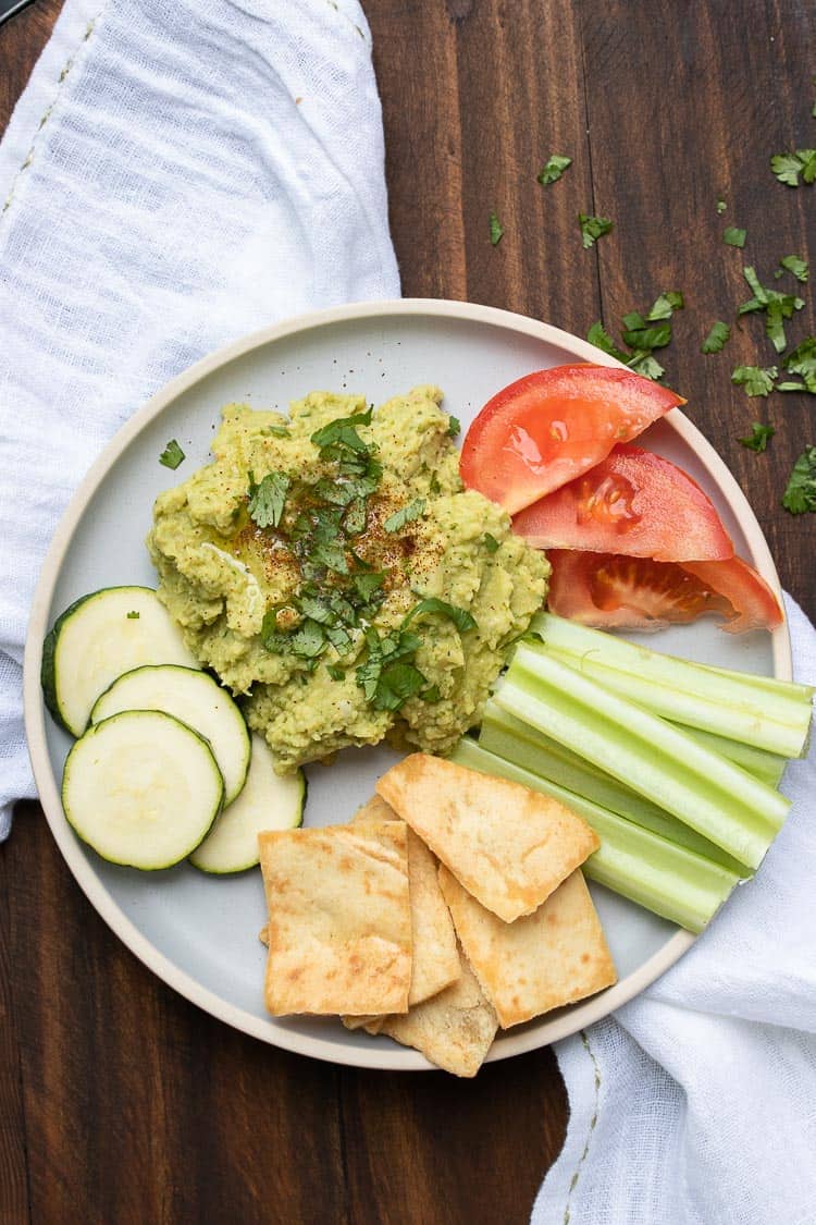 Grey plate with a pile of hummus surrounded by pita chips and veggies