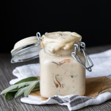 Front view tan creamy sauce with caramelized onions and sage in glass jar