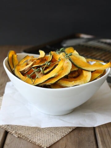 Baked Kabocha squash chips with thyme in a white bowl sitting on a wooden surface