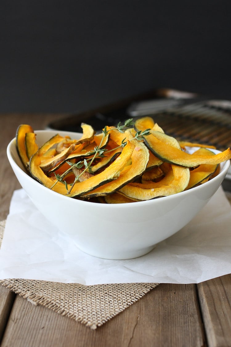 Baked Kabocha squash chips with thyme in a white bowl sitting on a wooden surface