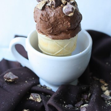 Chocolate ice cream topped with peanut butter cup crumbles in a cone sitting in a white mug.