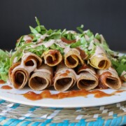 A side shot of vegan Rolled Tacos drizzled with hot sauce